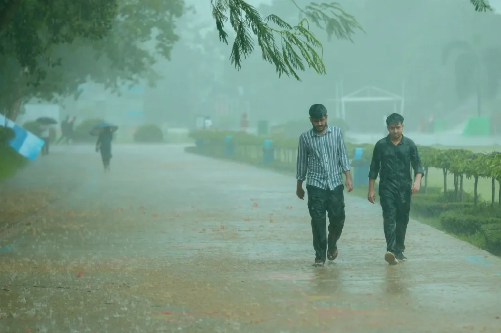 Deux hommes marchent sur un chemin de parc sous une forte pluie.
